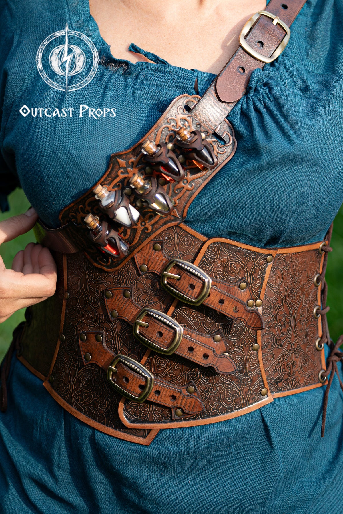 Person wearing a detailed leather harness with decorative elements, branded 'Outcast Props'. Embroidered Leather Underbust Corset – Elegant Brown Waist Cincher for Noble LARP Outfits, Steampunk and Fantasy Glamour