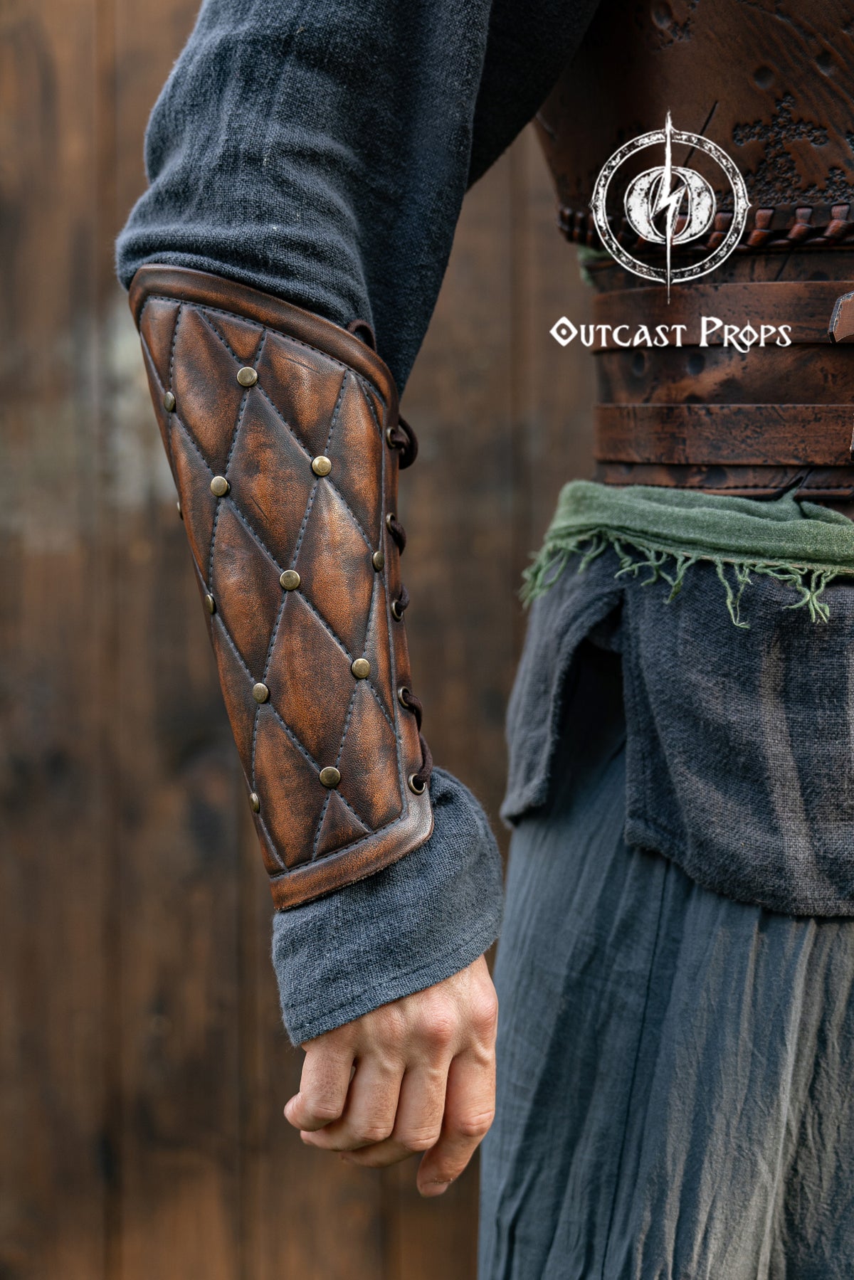 Close-up of a person wearing a detailed leather arm guard with 'Outcast Props' branding. Falken leather bracers for noble costume LARP outfit medieval fantasy accessories for Ren Faire cosplay arm guards for knight character gear