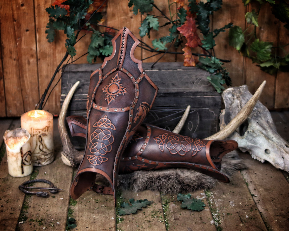 Handcrafted Celtic leather greaves displayed on fur with rustic candles and forest leaves, featuring embossed sun symbols and flowing knotwork inspired by the Rohirrim horsemen. Made from aged brown full-grain leather, riveted by hand with brass details and unique Outcast Props aging. Perfect LARP armor or medieval horseman cosplay accessory combining protection, artistry, and cinematic realism.