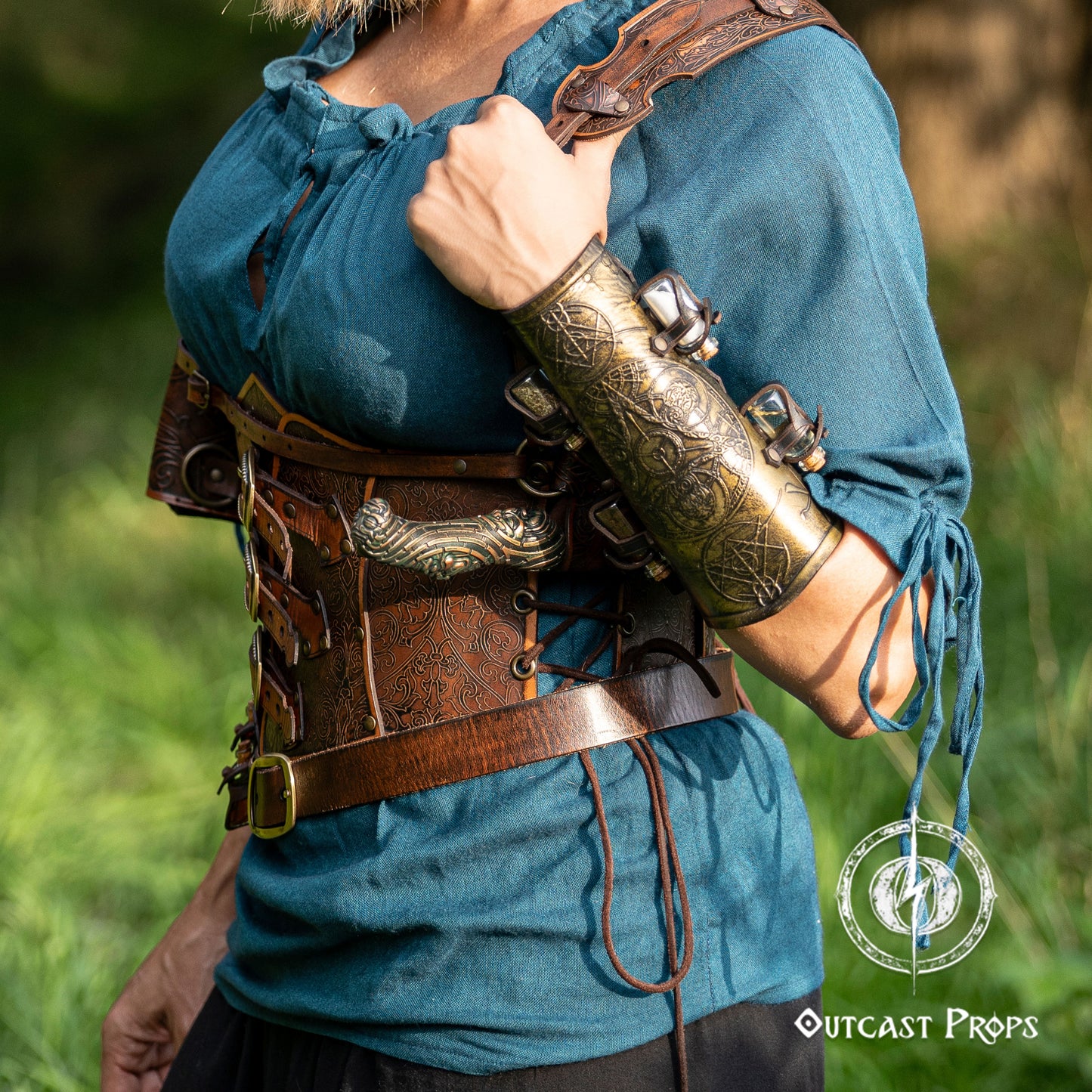 30 Plain leather belt. Person wearing a blue shirt with ornate arm guard and leather harness in a natural setting.