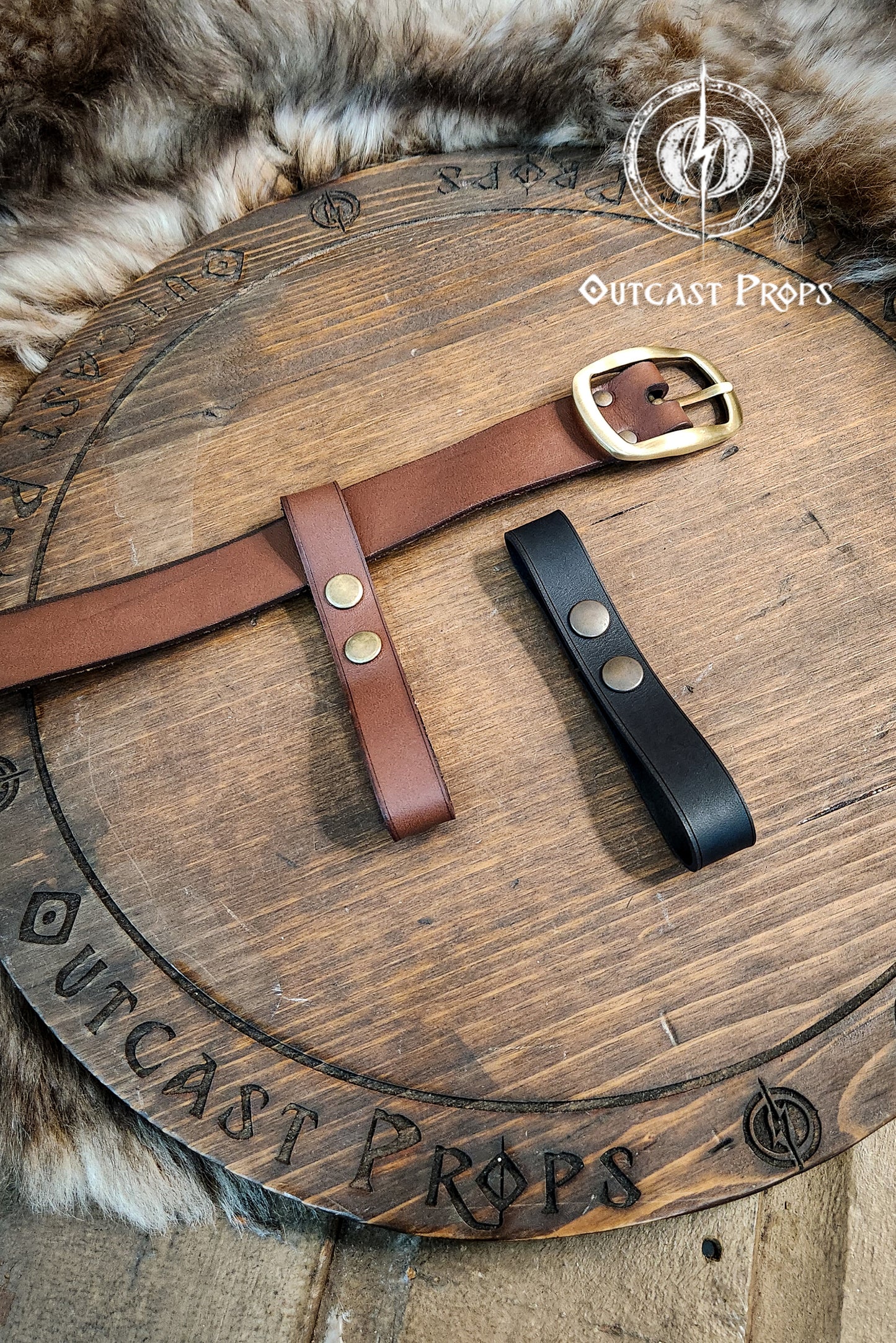 Two leather belts, one brown and one black, on a wooden surface with 'Outcast Props' branding. Versatile Leather Belt Clasp for LARP, Cosplay & Medieval Accessories - Handcrafted Vegetal Tanned Attachment