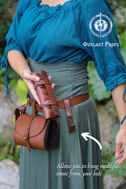 A woman in a teal blouse and green skirt demonstrates a brown vegetable tanned leather clasp attachment hanging from her belt during a LARP or Renaissance Faire styled shoot. She holds a cylindrical potion holster to show how the clasp can support additional accessories. The sturdy snap-fastened strap hangs freely, allowing mugs, pouches, wand holsters, scabbards or potion holders to be clipped securely. Ideal for LARP, cosplay and medieval outfits where modular gear is essential.