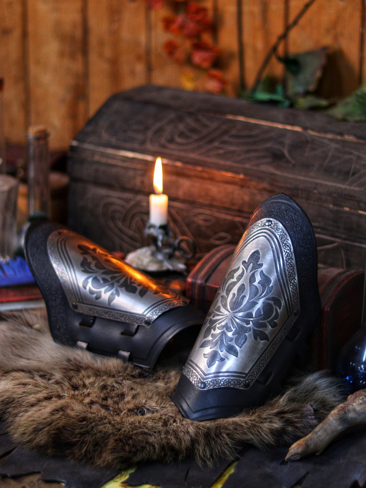 Bracers with engraved steel plates and black leather resting on fur beside a carved chest and candle. The perfect mix of noble elegance and fantasy gear, ideal for medieval roleplay, knight costumes, or detailed cosplay props. Rich warm tones enhance the immersive, handcrafted feel.