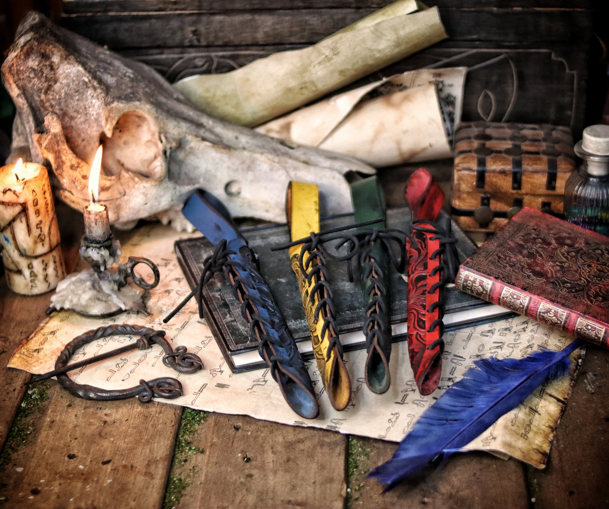 A close-up of an ornate laced leather wand holster displayed on a table with a decorative backdrop, featuring a leather-bound notebook and a candle. Magic Wand leather Holster Ornated Laced & Aged, for wizard and witch costume belt holster LARP and magic conventions and fair events