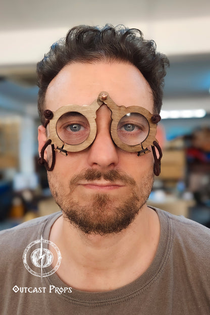 Man wearing a wooden medieval glasses with Outcast Props logo in the corner. Medieval eyeglasses steampunk glasses larp alchemist glasses renaissance fair eyewear medieval spectacles fantasy glasses cosplay accessory. Vintage-Inspired Alchemist Spectacles: Medieval LARP Steampunk Eyewear for Renaissance Fairs & Cosplay