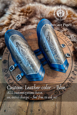 Blue leather arm guards with intricate designs on a wooden surface, featuring Outcast Props branding.