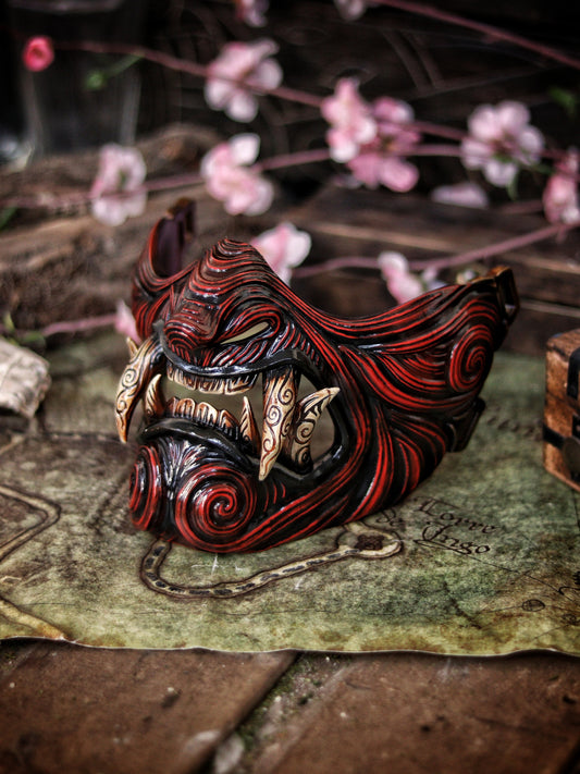 A hand-painted Oni Samurai Mempo mask with red and black details, displayed on a surface with a map background and pink flowers in the peripheral. Samurai oni mask japanese half oni mask samurai wearable mask for cosplay larp menpo mask scorpion clan mask l5r samurai mask