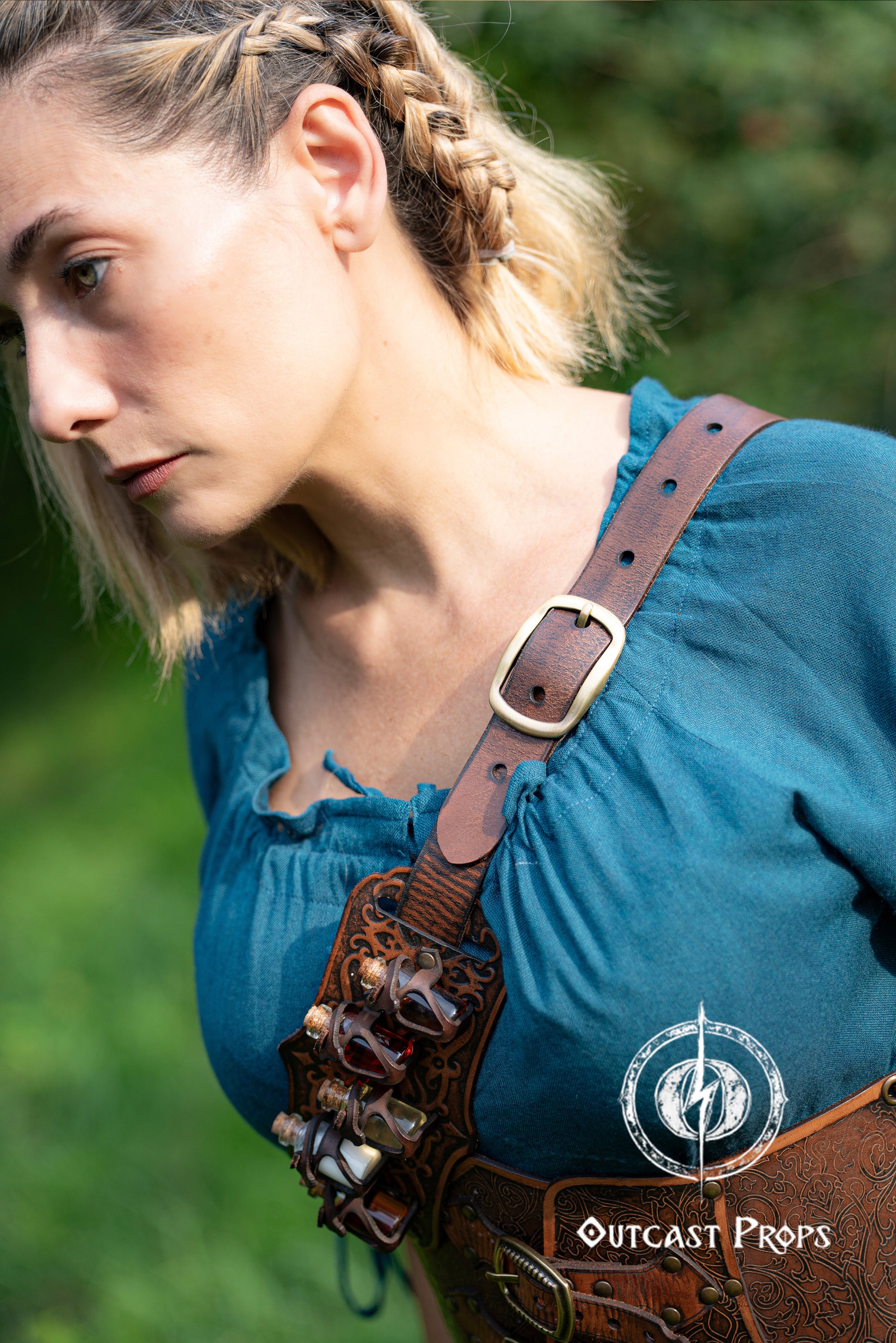 Person wearing a blue top with leather straps and Outcast Props logo in the corner. A handmade leather potion holder with ornate embossed patterns, designed to hold five small glass vials. The holder is displayed on a furry surface, and the vials have cork stoppers. Ornated Belt potion holder | 5  potion Belt carrier | LARP, cosplay, fantasy alchemist accessory, adventurers, steampunk, alchemist, healers