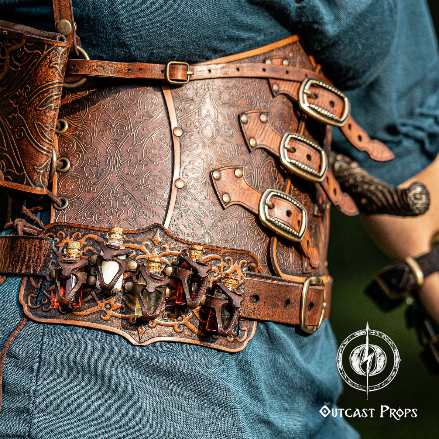 Close-up of a detailed leather belt with decorative elements and buckles, worn by a person. A handmade leather potion holder with ornate embossed patterns, designed to hold five small glass vials. The holder is displayed on a furry surface, and the vials have cork stoppers. Ornated Belt potion holder | 5  potion Belt carrier | LARP, cosplay, fantasy alchemist accessory, adventurers, steampunk, alchemist, healers