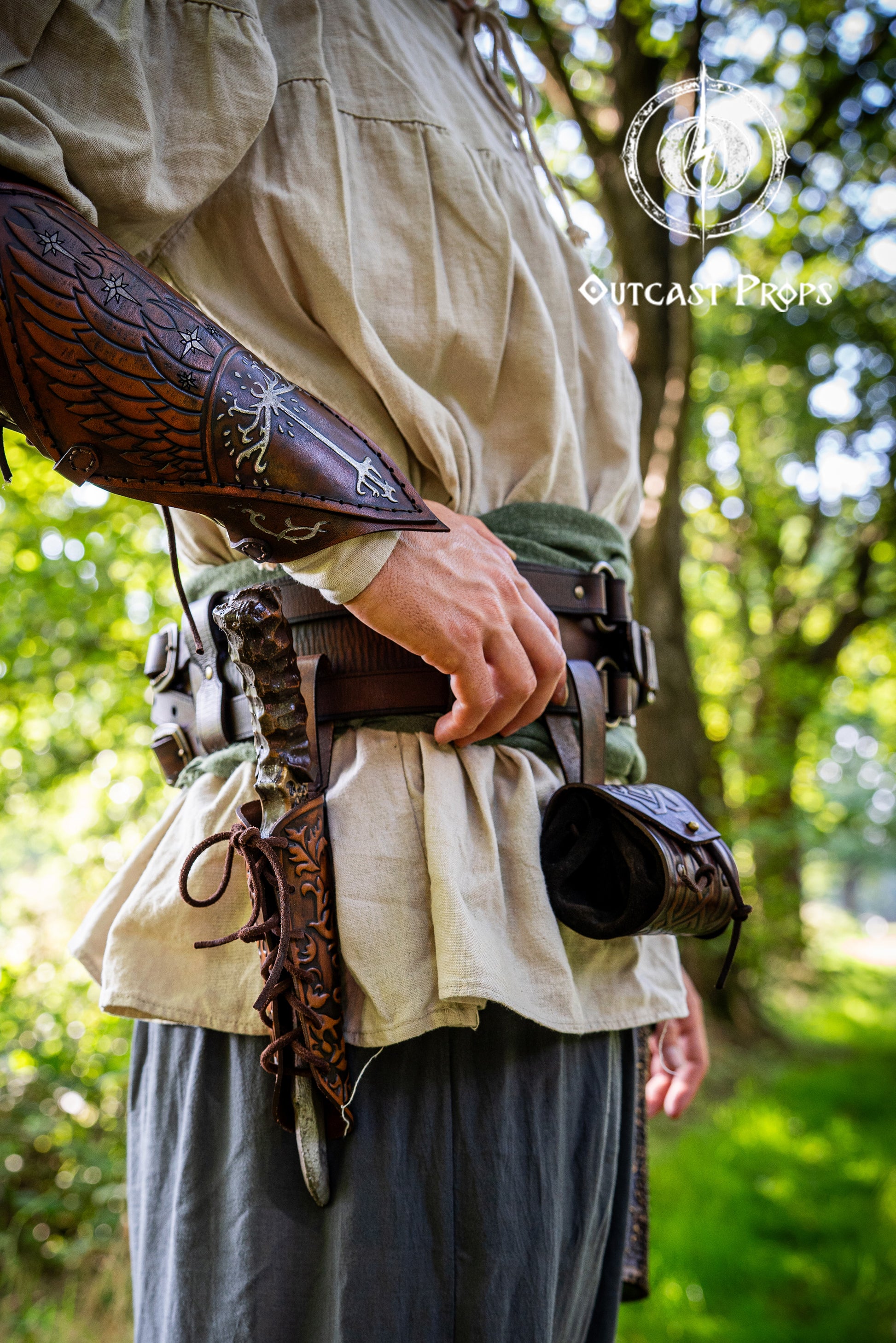 Person wearing period-appropriate armor and clothing in a forest setting, with 'Outcast Props' branding. Handmade leather dagger sheath | Ornate LARP scabbard | Viking, medieval, fantasy belt holster for daggers | Ren Faire cosplay accessory