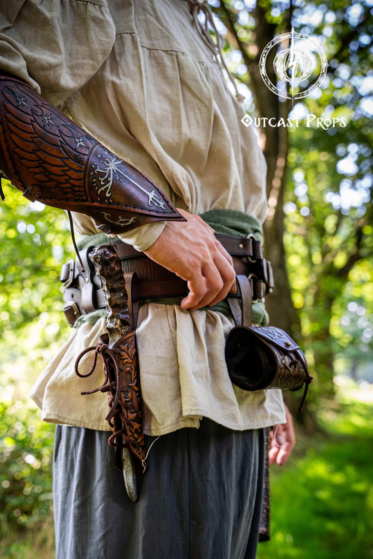 Person wearing period-appropriate armor and clothing in a forest setting, with 'Outcast Props' branding. Handmade leather dagger sheath | Ornate LARP scabbard | Viking, medieval, fantasy belt holster for daggers | Ren Faire cosplay accessory