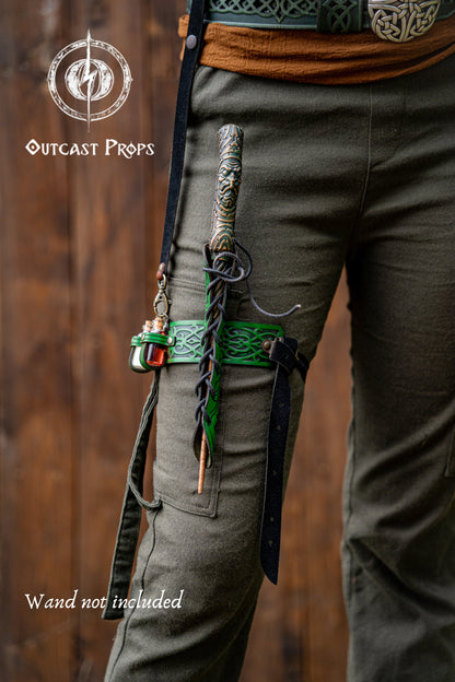 Person wearing green pants with a sword on a wooden background, featuring 'Outcast Props' branding. Cosplayer wears a green embossed leather wand holster garter with potion bottles and a rustic fantasy look. The wand holster wraps around the thigh, secured by adjustable straps. A perfect cosplay wand holder for witches, druids, or mages. The holster doubles as a larp potion holster, keeping tools of magic close. Designed for immersive fantasy costumes and magic users who attend LARP, Ren Faires or wizard