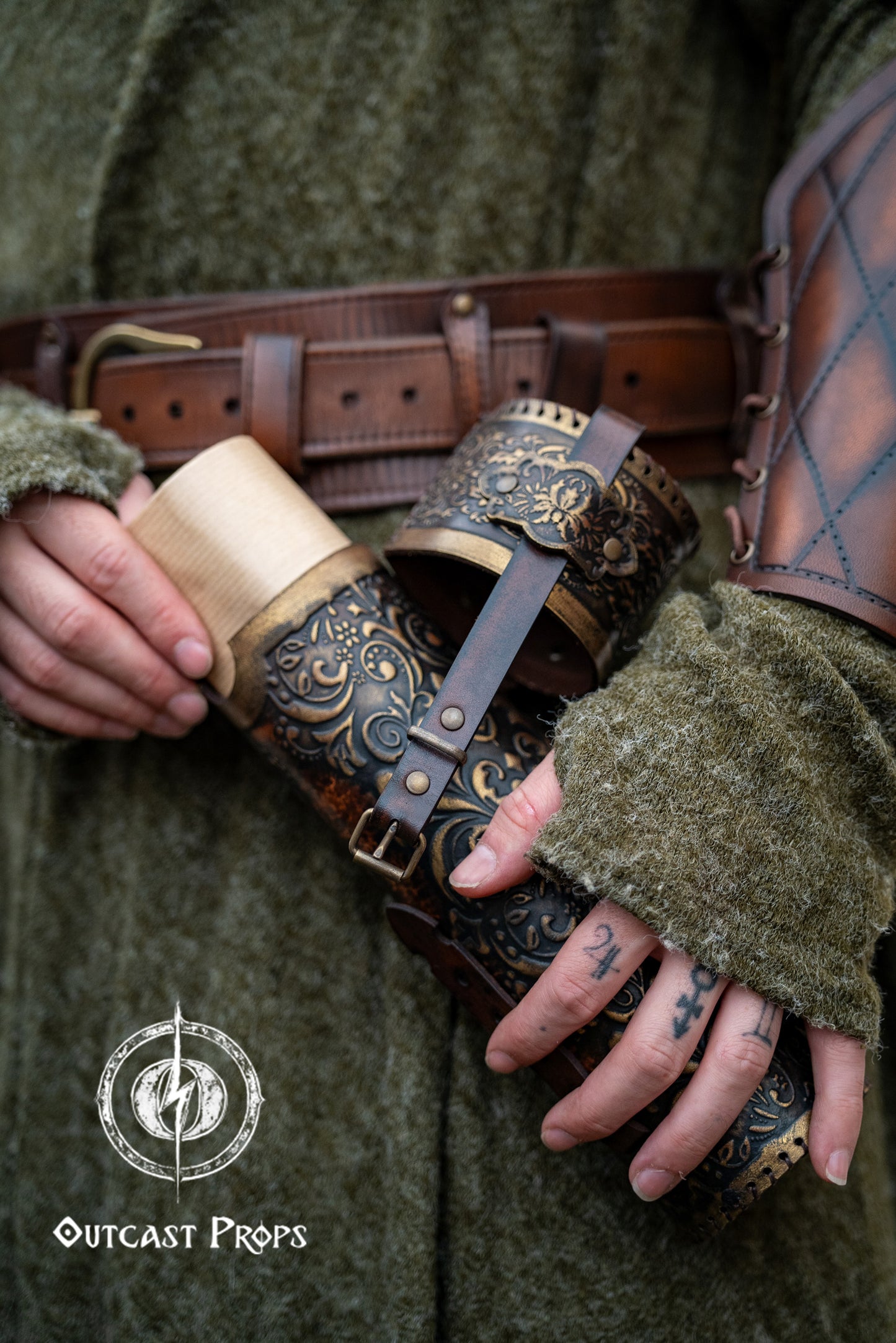 Detailed view of a fantasy scroll case being opened, revealing rolled parchment inside. The leather case is brown with golden embossed decorations, worn on the hip of a medieval-style outfit with matching bracers. Perfect LARP and Renaissance fair accessory for mages, scholars, or witches. Handcrafted with vegetable-tanned leather, perfect for storing maps, secret documents or magical scrolls.