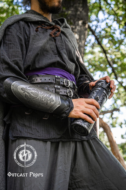 Medieval character in dark clothing and a purple sash holding a silver-embossed black leather scroll case. The character wears matching engraved bracers and a double belt, suggesting a noble or wizard persona. Ideal for fantasy roleplay, LARP, or Renaissance fair costumes. Leather is vegetable-tanned and hand-dyed, with intricate floral engraving. Functional and stylish scroll storage. Exquisite document tube for cosplay and LARP, Messengers, Magicians, steampunk, reanaissance, fantasy costumes.