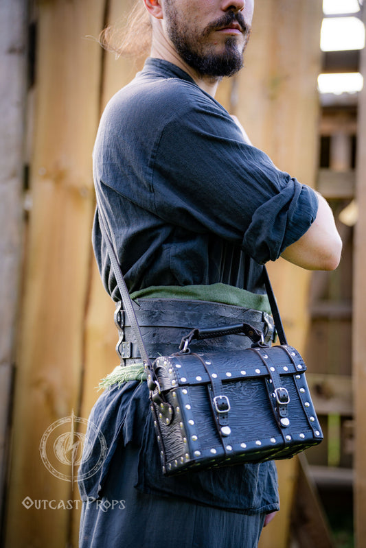 Man wearing a pirate chest leather bag with studs, standing outdoors. Leather treasure chest pirate chest bag larp pirate backpack treasure chest purse pirate accessories cosplay renfaire pouch belt bag