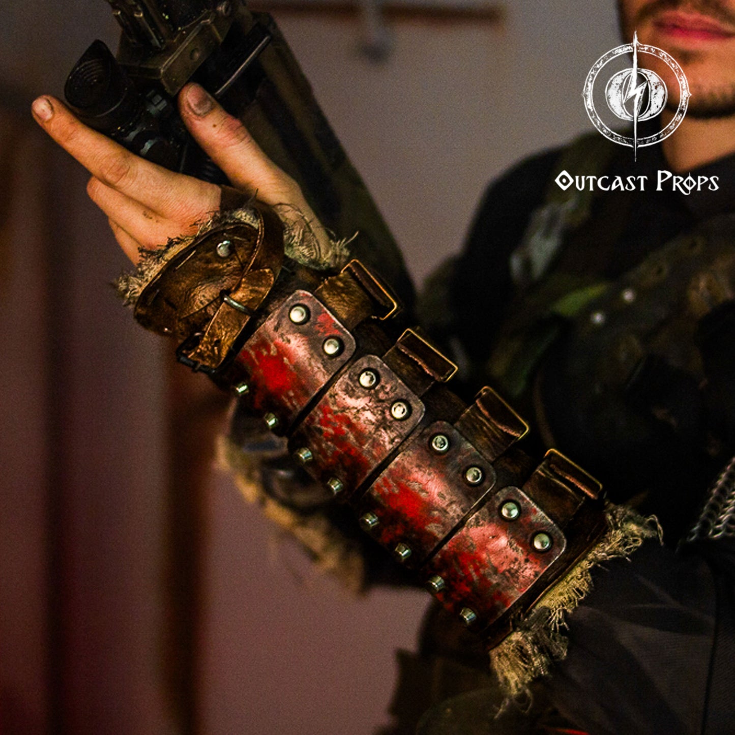 Handmade leather and metal bracer with red painted finish and oxidized steel rivets, shown on a costumed survivor holding a weapon. The arm guard fits over tattered costume fabric, highlighting its battle-worn, handcrafted aesthetic. Ideal for wasteland cosplay, dieselpunk gear, or immersive LARP builds. A perfect accessory for grim scavengers or road warriors. Dystopian Leather & Steel Bracer: Post-Apocalyptic Arm Guard for Wasteland Cosplay and LARP