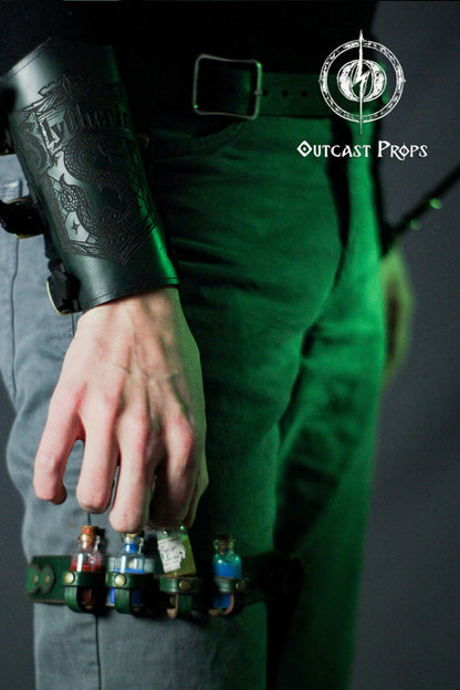 A green leather leg strap with a metal buckle and four small glass vials with cork stoppers. The strap has a metal ring and a green leather strap attached to it. The strap is decorated with a metal charm. The strap is worn on a person's leg. The vials contain red, blue, and clear liquids. Potion Garter Holster made of natural leather with bottles. Larp. Steampunk. Witch. Alchemy. Occult. Medieval. Cosplay. Many colors. Unisex.