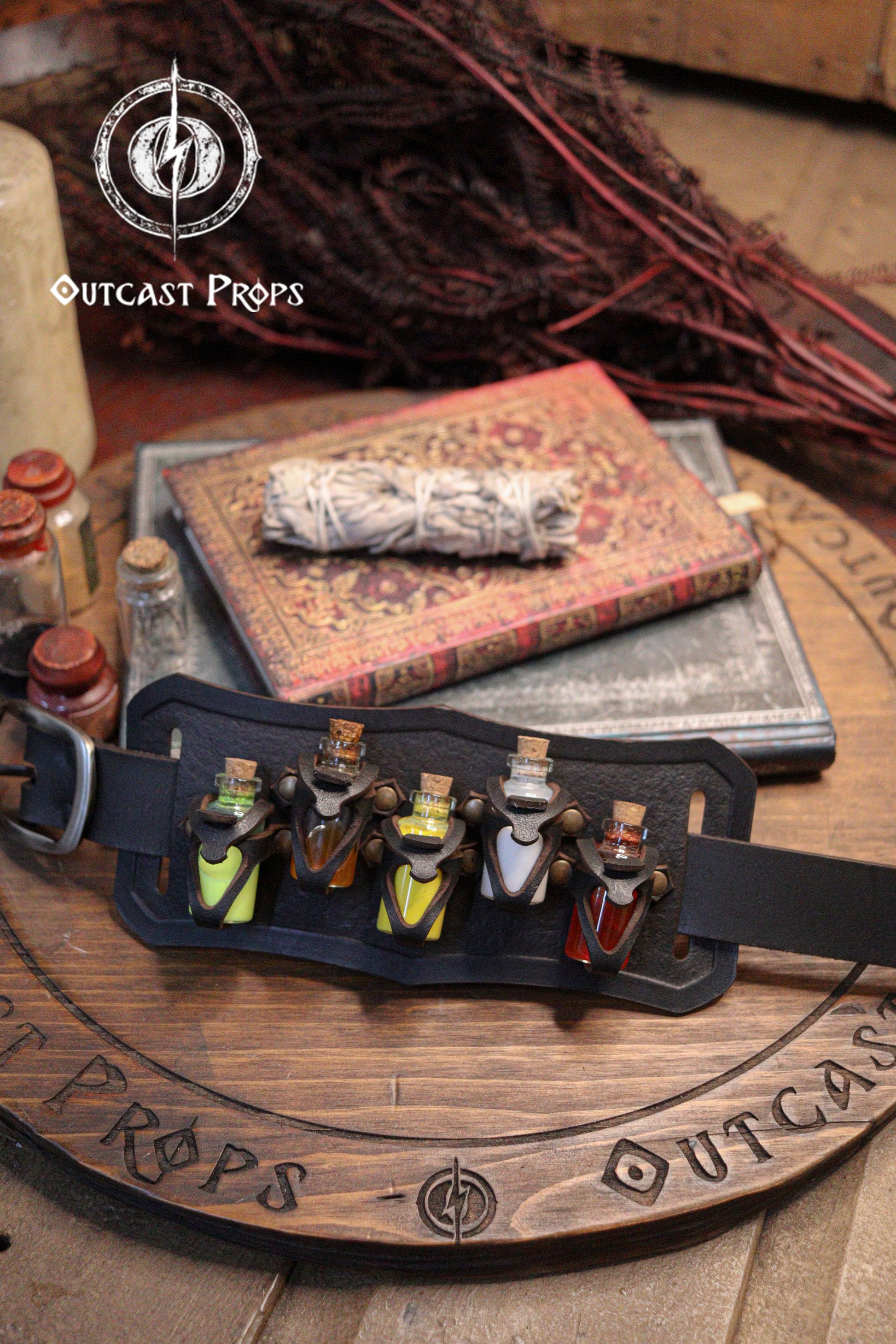 Belt Potion holder for 5 small bottles. Made of leather for adventurers, steampunk, alchemist, healers, cosplay or just to keep spices. Belt with small potions on a wooden surface with 'Outcast Props' branding.