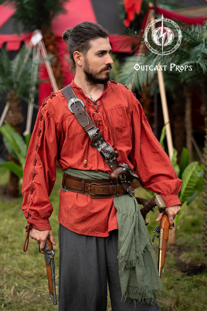 Full pirate outfit with a red shirt, green sash and pirate baldric for 4 flintlock pistols and a sword. Designed for Jack Sparrow fans and pirate reenactors, this silver-engraved leather piece is ideal for LARP, renaissance fairs, cosplay and themed photoshoots. Inspired by Blackbeard and historical pirates, handmade with premium vegetable-tanned leather for an authentic pirate look at any fantasy or Halloween event. Man in historical reenactment attire with weapons and props, standing outdoors.