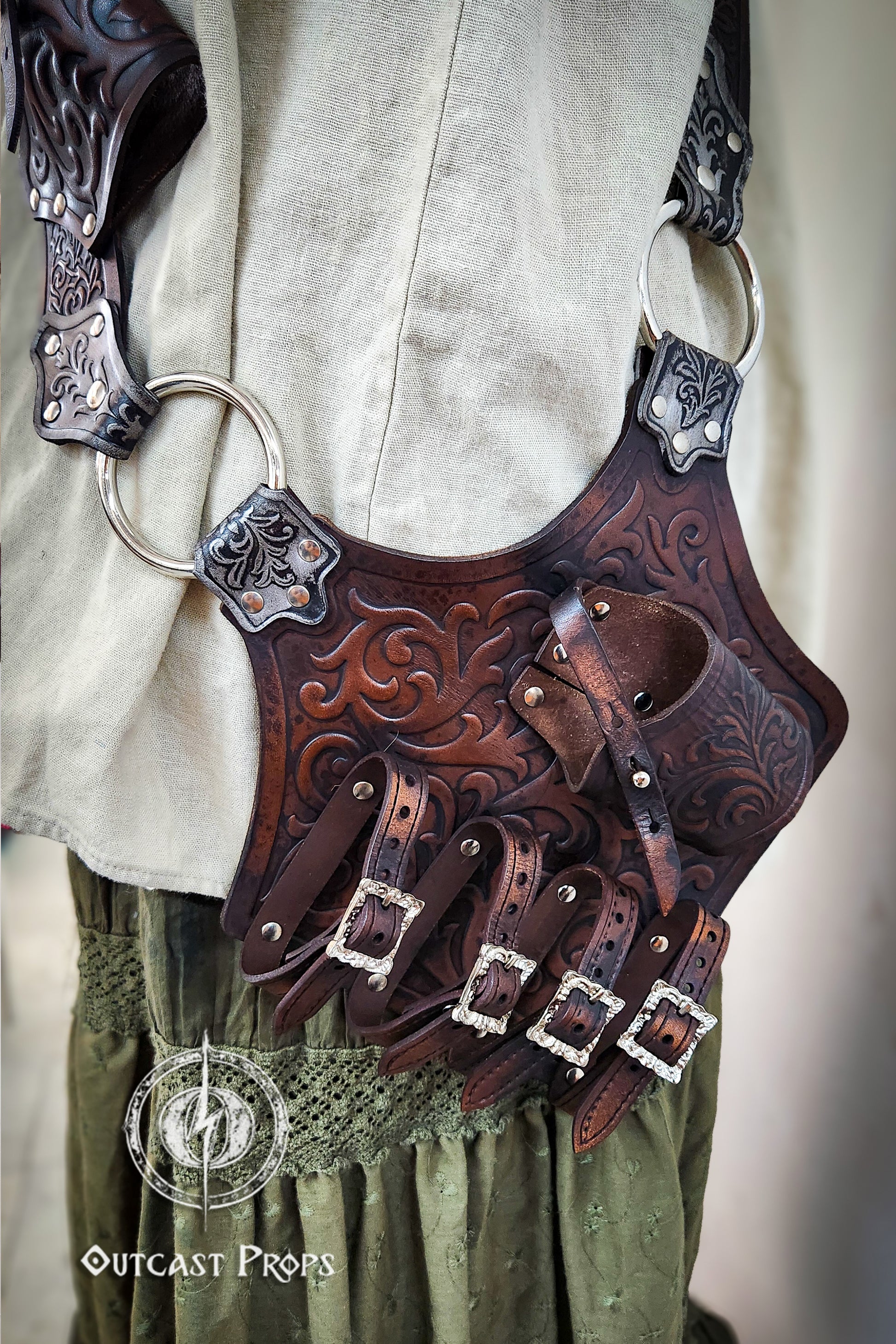 Decorative leather belt with intricate designs worn over a light-colored shirt and green pants. Pirate baldric for 4 flintlock pistols and a sword, inspired by Blackbeard, Anne Bonny, Captain Kidd and Pirates of the Caribbean. Ideal for LARP, Renfaire, renaissance fair, Pirate Weekend, cosplay, Halloween and Black Sails. Silver-engraved leather, handmade with vegetable-tanned leather. Premium pirate shoulder belt for Jack Sparrow costume, historical reenactment and fantasy events. High quality pirate access