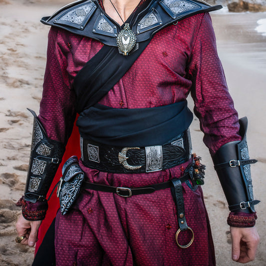Person wearing a detailed costume with red shirt, black shoulder guards, and armor accents. Ramattush Persian Leather Broadbelt, ornamental Arabic and Persian courts inspired, larp oriental leather belt, fantasy belt, renfaire belt