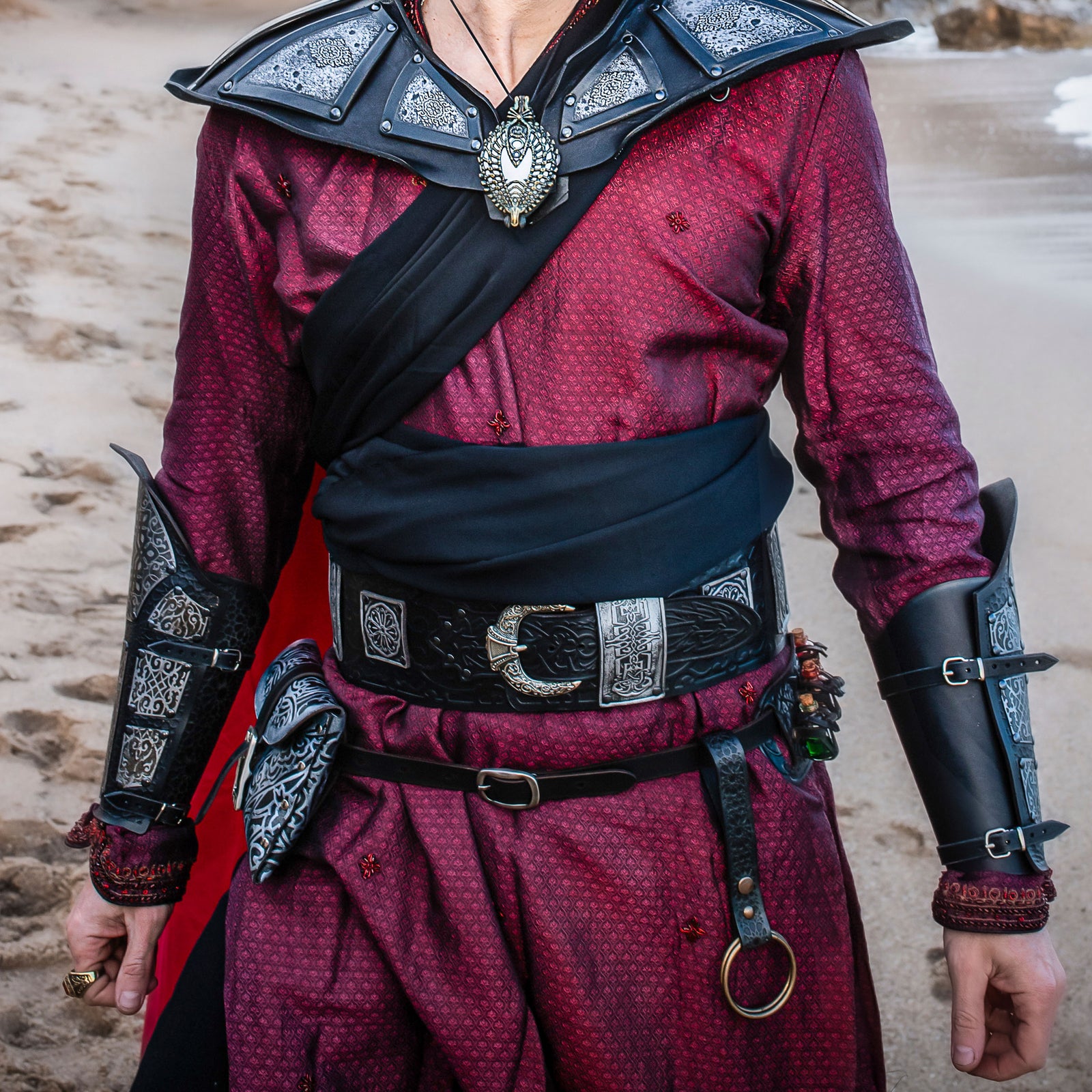 Person wearing a detailed costume with red shirt, black shoulder guards, and armor accents. Ramattush Persian Leather Broadbelt, ornamental Arabic and Persian courts inspired, larp oriental leather belt, fantasy belt, renfaire belt
