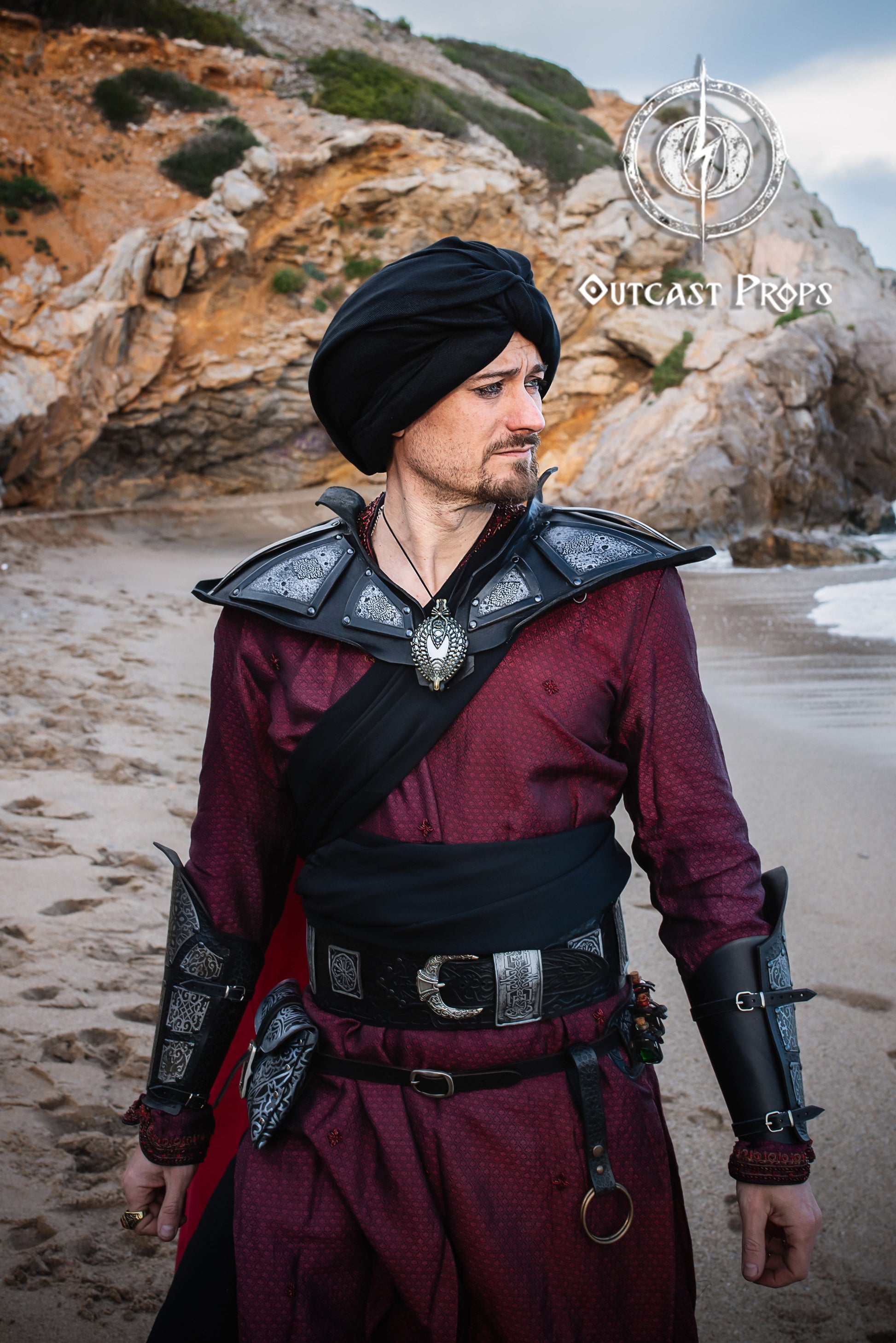 Man in medieval armor standing on a rocky beach . LARP character in Arabic-inspired costume wearing the wide leather belt with matching vambraces. The black leather belt stands out with its silver plates. Ideal image for keywords like black leather belt, larp belt, and belt for costume.