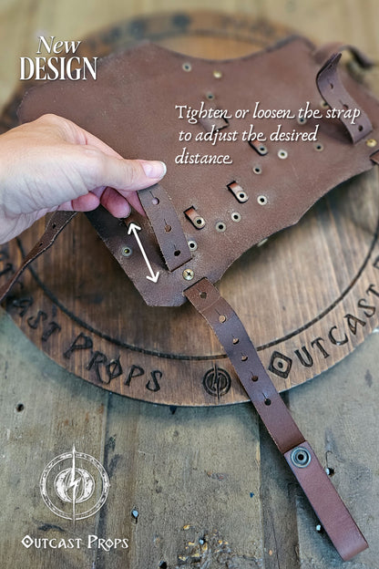 Underside view of the brown leather leg holster showing the adjustable strap system. A hand demonstrates tightening or loosening to modify distance from the waist. Crafted with precision stitching and brass rivets on a wood Outcast Props board. Handmade from premium vegetable-tanned leather, perfect for LARP, cosplay, and renaissance fair costumes. Designed for rogues and alchemists who value durability, realism, and adjustability.