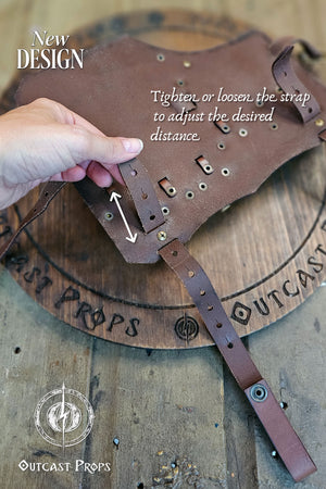 Underside view of the brown leather leg holster showing the adjustable strap system. A hand demonstrates tightening or loosening to modify distance from the waist. Crafted with precision stitching and brass rivets on a wood Outcast Props board. Handmade from premium vegetable-tanned leather, perfect for LARP, cosplay, and renaissance fair costumes. Designed for rogues and alchemists who value durability, realism, and adjustability.