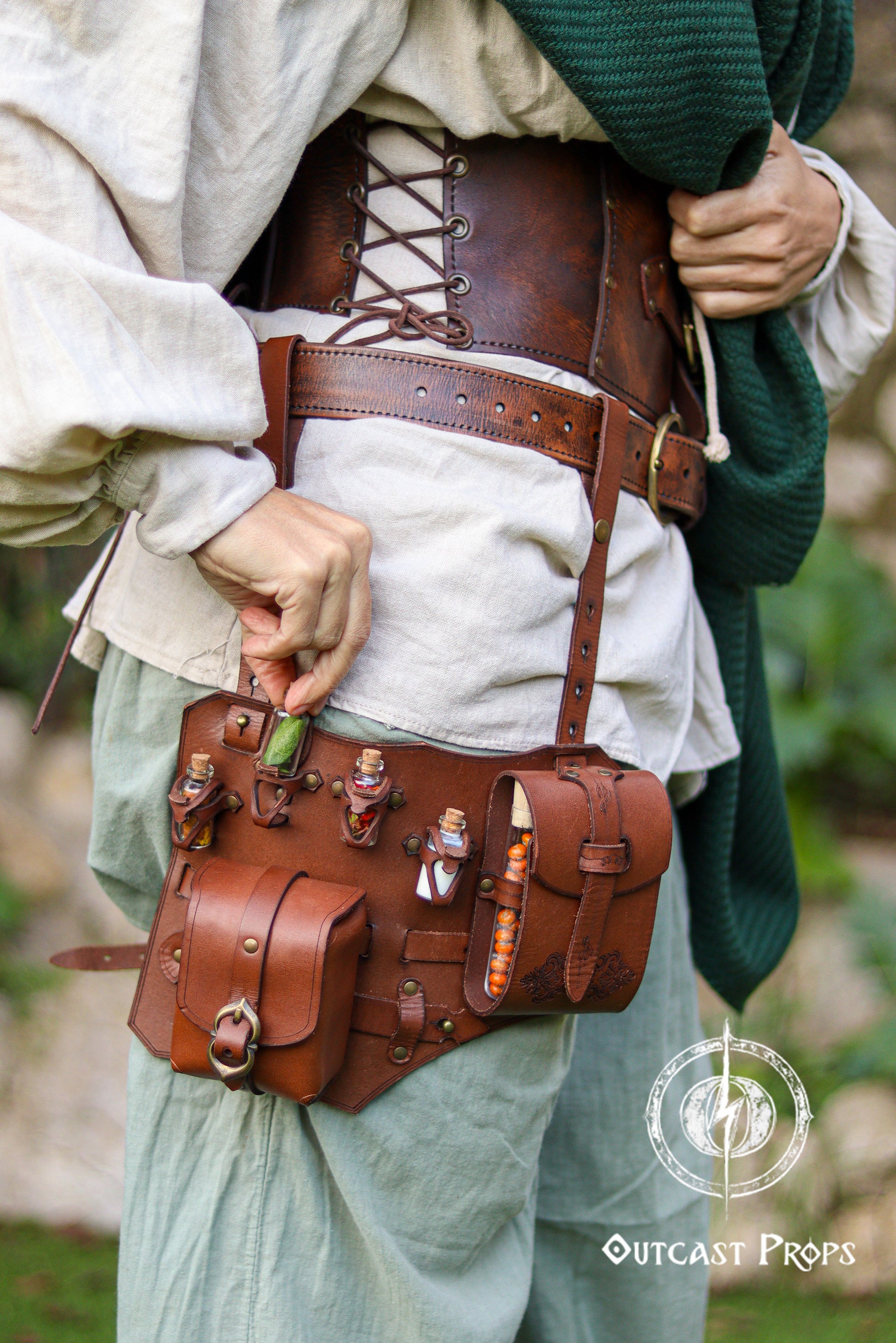 Close up of the upgraded leather leg harness potion belt worn over loose fantasy trousers. The shot highlights the modular design with reinforced straps, thigh attachment, potion vials in carved holders and a book holster style side pocket. Rich brown vegetable tanned leather with aged finish evokes steampunk and alchemist gear. Ideal for LARP adventurers, rogues and herbalists who need a functional larp belt or potion belt that keeps essentials secure during movement.
