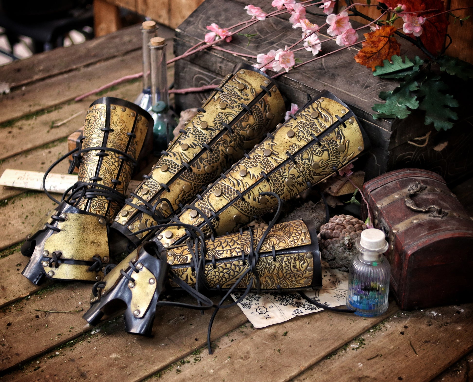 Flat-lay of complete set: samurai leather greaves and bracers with dragon engravings, arranged with potions, scrolls, and fantasy props. Rich context for fantasy costume leg armor, perfect for cosplay or L5R events. Designed to assist visually impaired users with setting and content.