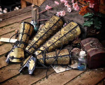 Flat-lay of complete set: samurai leather greaves and bracers with dragon engravings, arranged with potions, scrolls, and fantasy props. Rich context for fantasy costume leg armor, perfect for cosplay or L5R events. Designed to assist visually impaired users with setting and content.