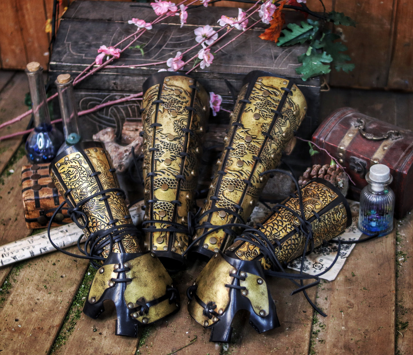 Flat-lay of complete set: samurai leather greaves and bracers with dragon engravings, arranged with potions, scrolls, and fantasy props. Rich context for fantasy costume leg armor, perfect for cosplay or L5R events. Designed to assist visually impaired users with setting and content.