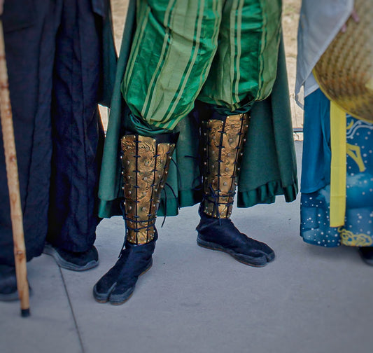 Zoom on greaves with embossed oriental dragon patterns worn over black split-toe boots, part of a green samurai costume for fantasy events or LARP. The leather armor is hand-dyed and riveted, designed for durability and visual impact.