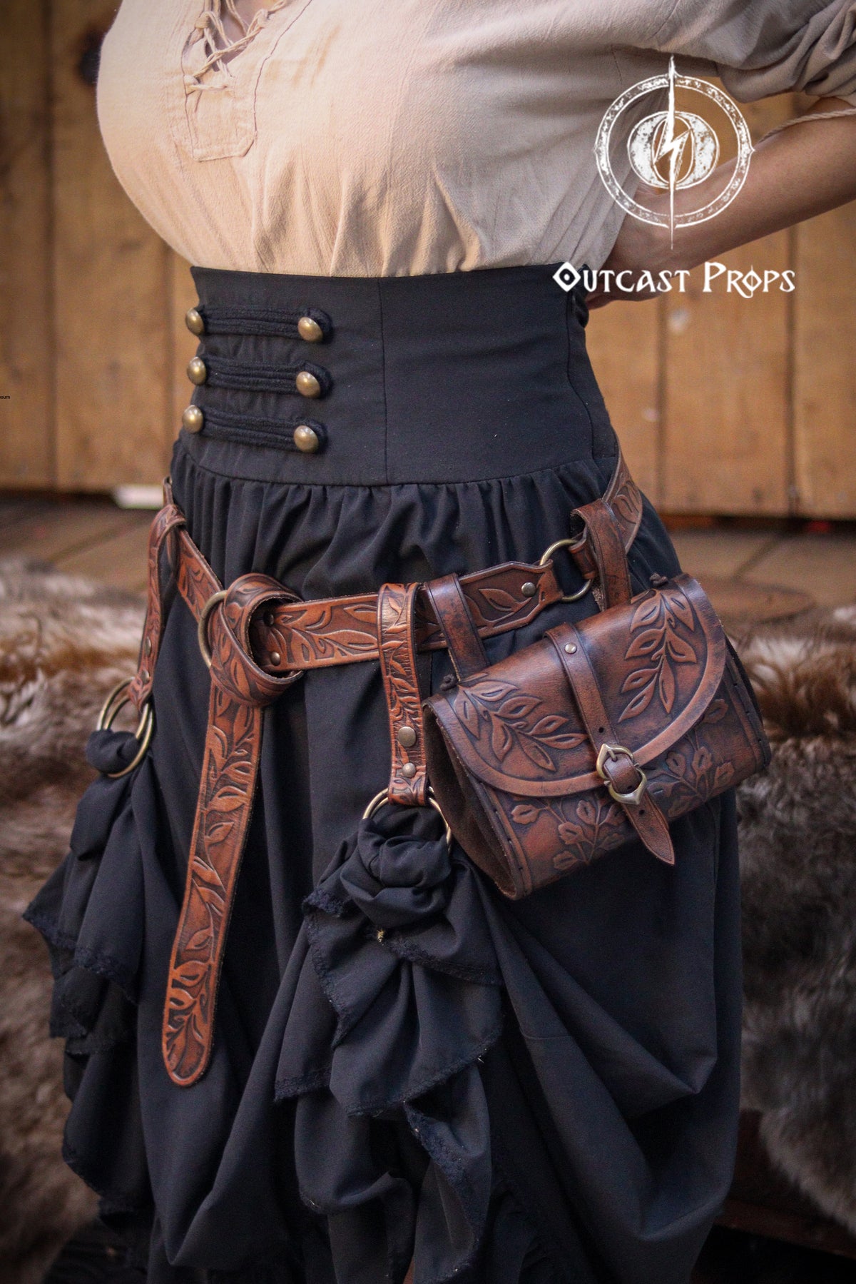 A black skirt with a brown leather belt and a brown leather pouch with floral designs. The belt has metal buckles and rings. The pouch has a flap with a metal buckle. The skirt has a high waist and is cinched in with a black fabric belt with metal buttons.  Floral Leather Skirt Hike Ring LARP Ren Faire Cosplay Accessory for Fantasy Outfits Skirt Hiker Renaissance Fair Costume Accessory