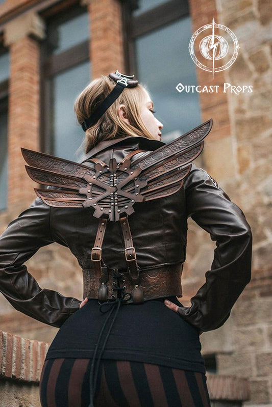 Person wearing a black leather outfit with winged design in front of a brick building, branded 'Outcast Props'. Steampunk Wings leather gears fairy victorian outfit burning man aviator pin up costume clock