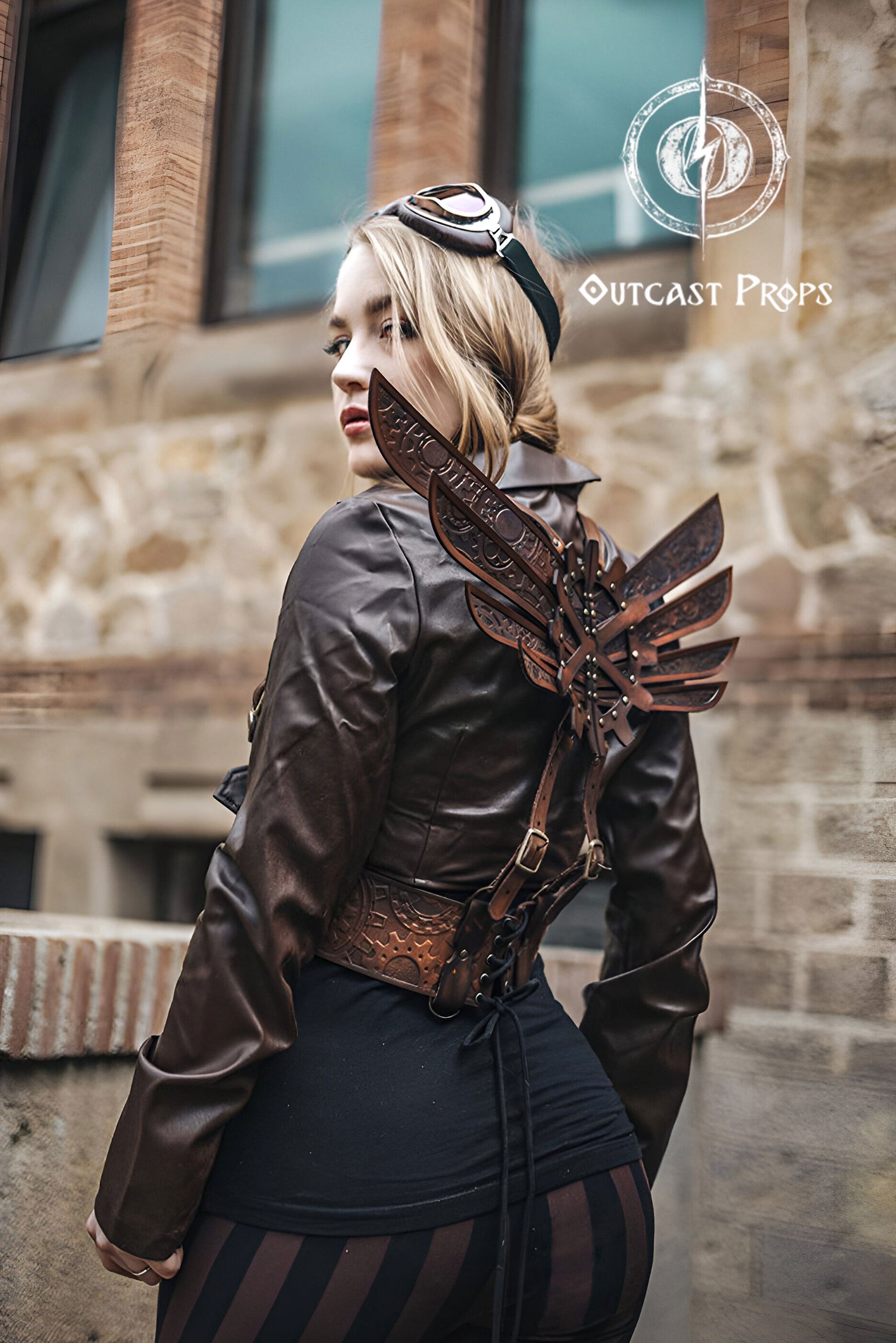 Person wearing a steampunk-style leather jacket with decorative elements, standing against a stone building. Steampunk Wings leather gears fairy victorian outfit burning man aviator pin up costume clock