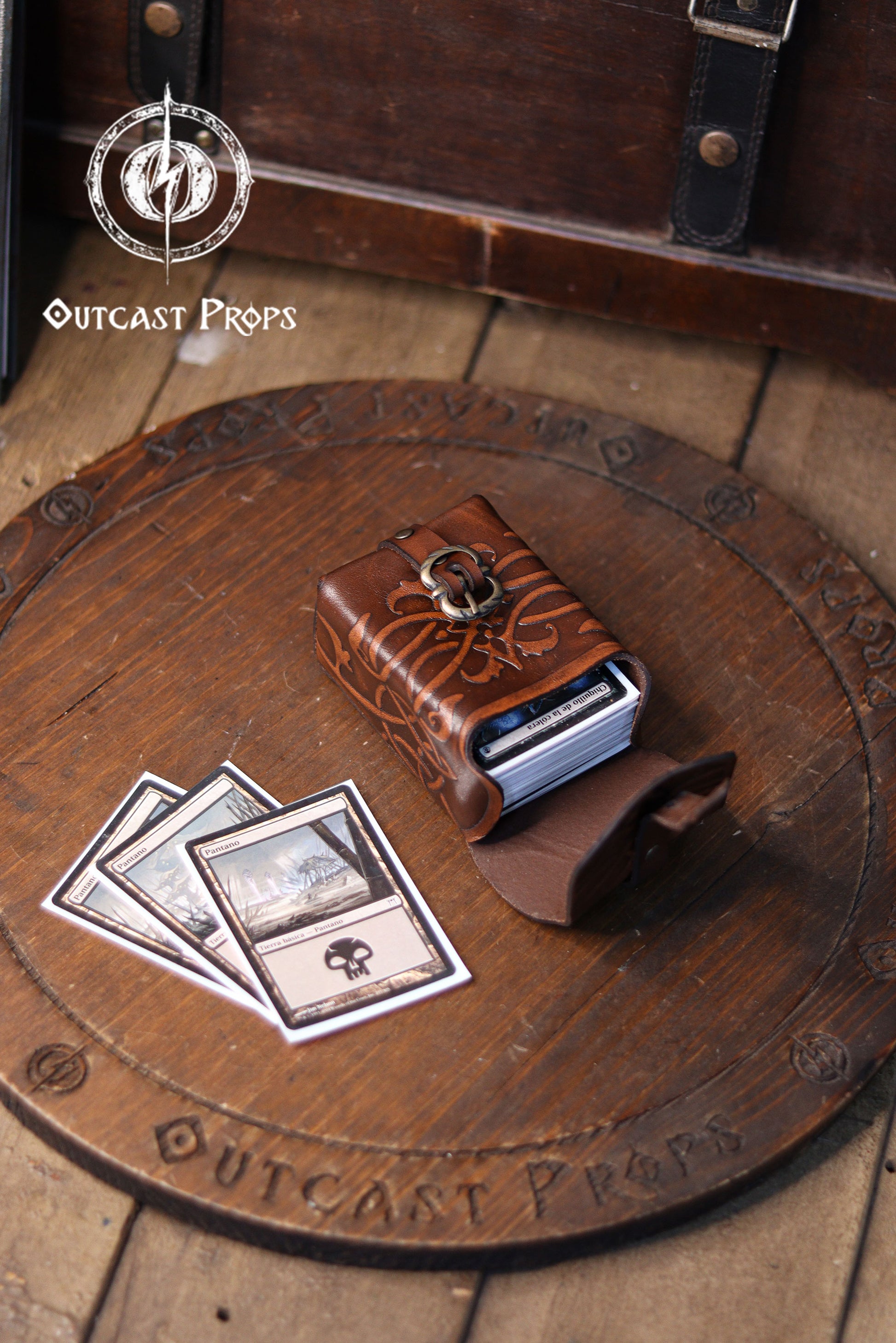 Handcrafted ornated leather tobacco bag made from premium vegetable-tanned leather, shown open on a wooden surface holding a deck of trading cards. This medieval leather belt pouch features embossed floral patterns, brass buckle closure, and compact structure. Ideal as a unique handmade gift, leather deck holder for Magic the Gathering, Pokémon or Arkham Horror cards, or an elegant everyday belt pouch.