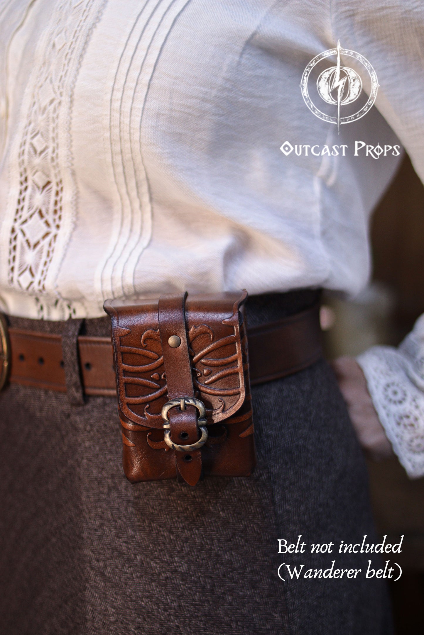 Close-up of an ornated medieval leather tobacco bag attached to a belt, showing embossed floral patterns, hand-dyed finish, and solid brass buckle. Crafted from premium vegetable-tanned leather, this compact belt pouch is ideal for everyday use, tabletop card games, or as a thoughtful handmade leather gift for fantasy, steampunk, or Renaissance fair enthusiasts. Close-up of a belt with decorative buckle worn by a person, with 'Outcast Props' branding.