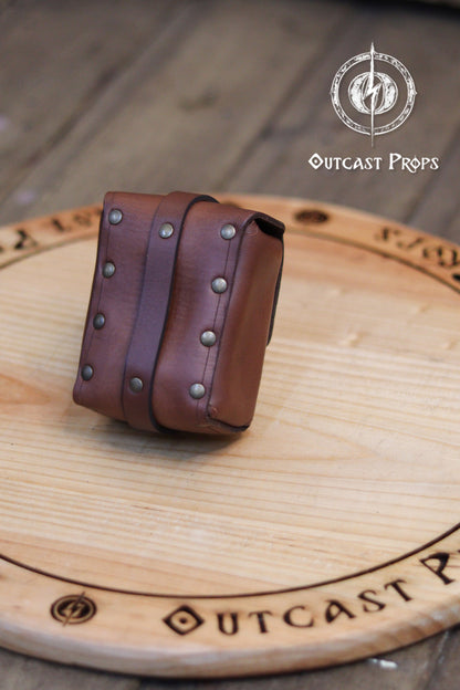 Tavern Small Leather Belt Pouch for Daily Wear LARP Renaissance Fair Viking Cosplay Medieval Accessory Steampunk Coin or Tobacco Pouch. Brown leather belt with studs on a wooden surface, featuring 'Outcast Props' branding.