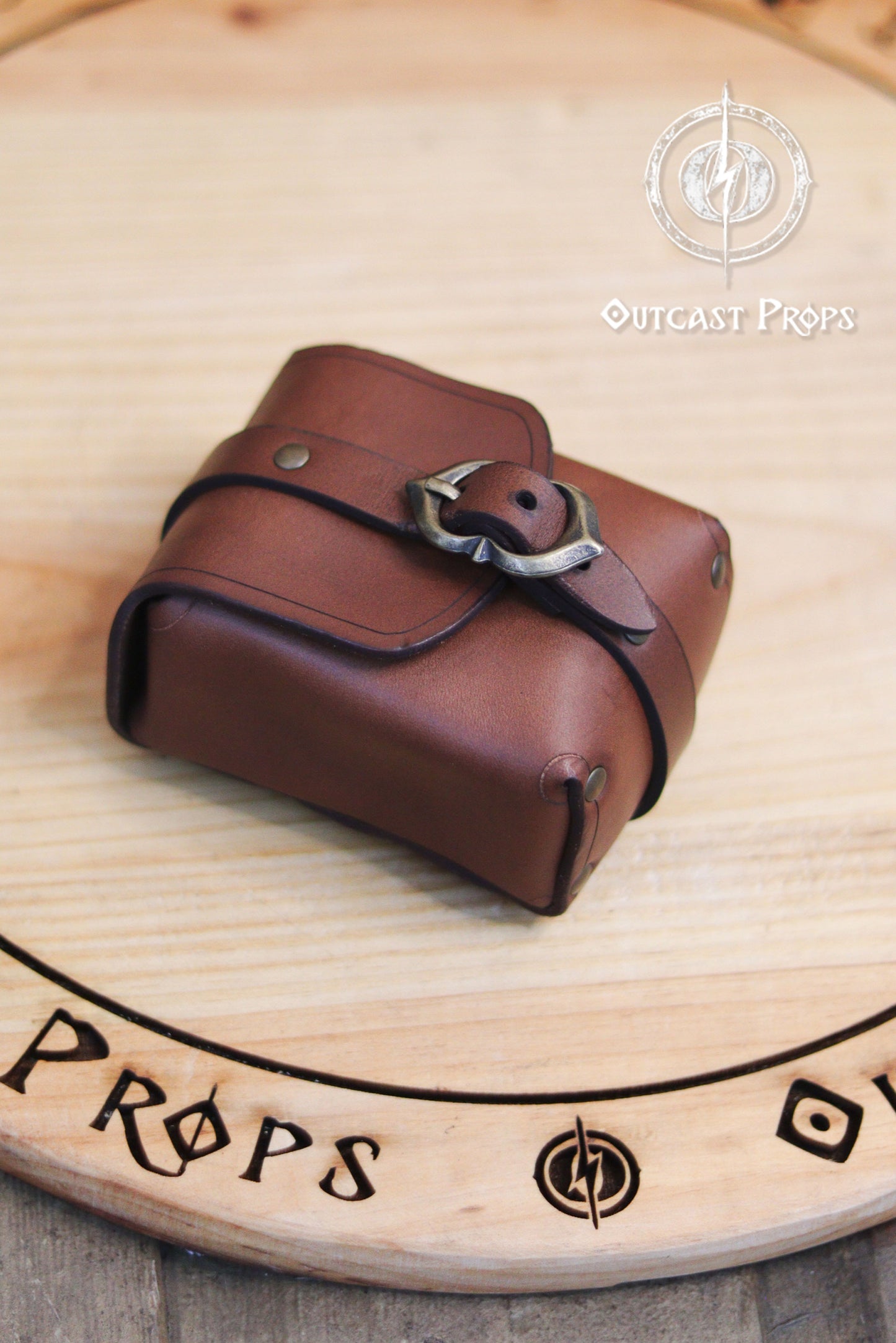 Tavern Small Leather Belt Pouch for Daily Wear LARP Renaissance Fair Viking Cosplay Medieval Accessory Steampunk Coin or Tobacco Pouch. Brown leather pouch with a buckle on a wooden surface, featuring 'Outcast Props' branding.