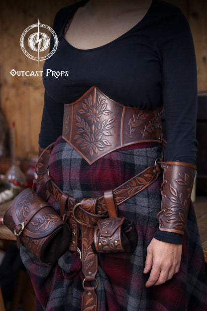 Full outfit view featuring the floral leather underbust corset belt worn with matching bracers and belt pouches. The embossed botanical design and aged brown finish create an elegant renaissance faire silhouette. Ideal for herbalist cosplay, elven characters, witchcore outfits and LARP costumes. The corset enhances the waistline without restricting movement, blending comfort with handcrafted fantasy style.