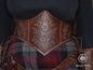 Front view of the floral leather underbust corset belt showing the detailed embossing and elegant curved shape that defines the waist and enhances the bust. The aged brown leather pairs with a plaid fantasy skirt and matching floral belt accessories. Ideal for renaissance faire outfits, elven cosplay, witchcore style, herbalist characters and LARP costumes. The handcrafted finish gives it a cinematic fantasy look.