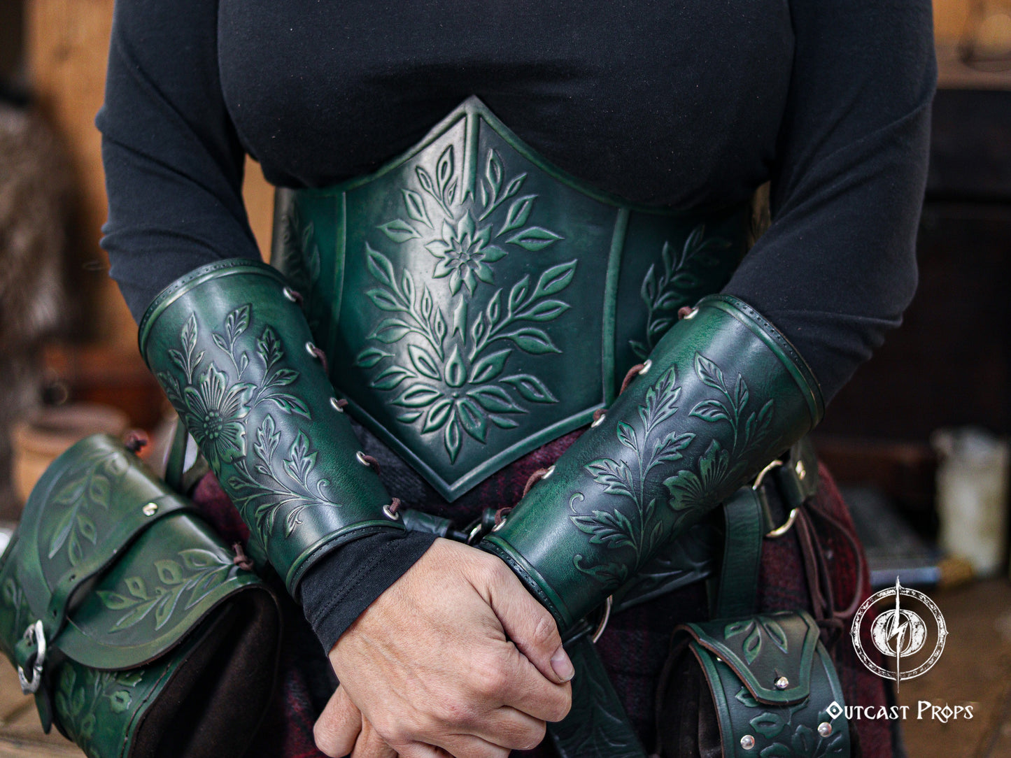 The model wears the green floral leather underbust corset belt together with matching bracers and belt pouches, forming a complete botanical themed outfit. The embossed floral patterns and rich green dyes evoke elven, druidic and herbalist aesthetics perfect for LARP events and renaissance faires. The handcrafted aged finish and coordinated accessories give the set a deep fantasy look inspired by enchanted forests.