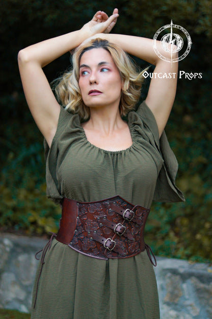 Woman wearing a green dress with a brown leather corset belt, standing outdoors. Elegant Floral Underbust Leather Corset - Handcrafted Rose Design for Larp, Reinassande Faire &amp; Cosplay
