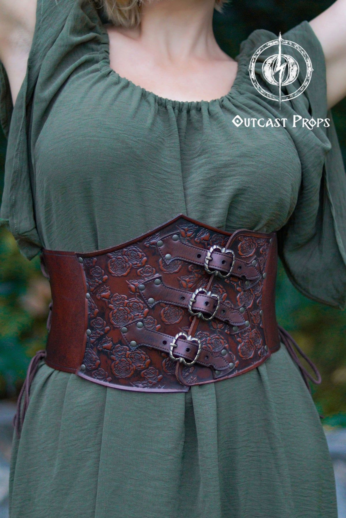 Person wearing a green dress with a brown leather corset belt, branded 'Outcast Props'. Elegant Floral Underbust Leather Corset - Handcrafted Rose Design for Larp, Reinassance Faire Cosplay