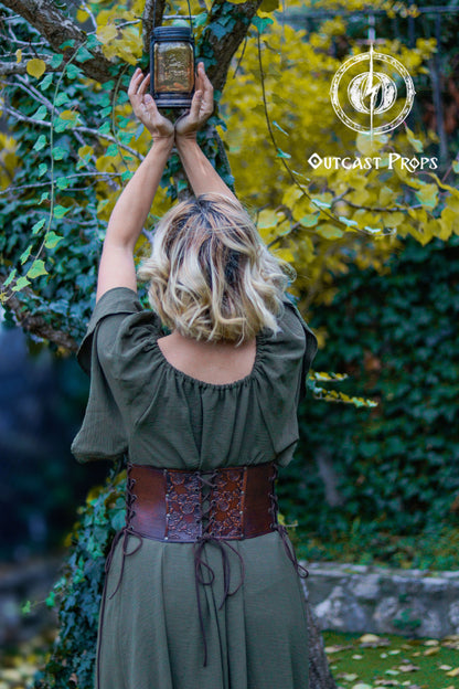Person holding a lantern in an outdoor setting with greenery. Elegant Floral Underbust Leather Corset - Handcrafted Rose Design for Larp, Reinassance Faire Cosplay