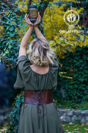 Person holding a lantern in an outdoor setting with greenery. Elegant Floral Underbust Leather Corset - Handcrafted Rose Design for Larp, Reinassance Faire Cosplay