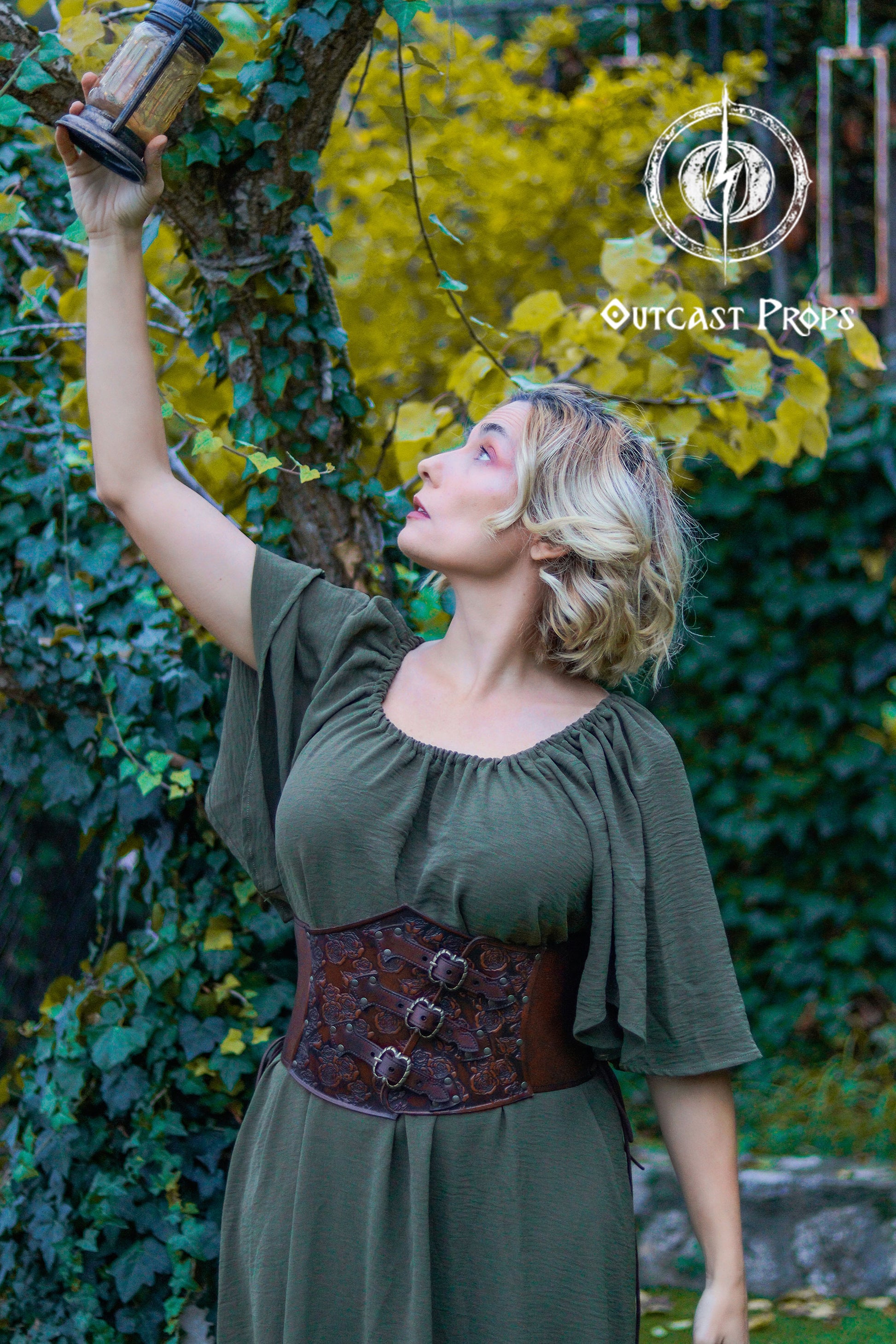 Woman in a green dress with a brown corset holding a lantern against a leafy background, with 'Outcast Props' branding. Elegant Floral Underbust Leather Corset - Handcrafted Rose Design for Larp, Reinassance Faire Cosplay