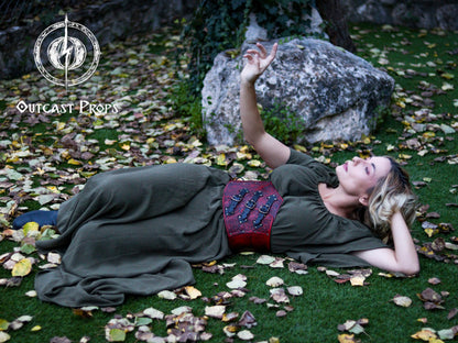 Person in a green dress with a red belt lying on grass with leaves and rocks. Elegant Floral Underbust Leather Corset - Handcrafted Rose Design for Larp, Reinassance Faire Cosplay